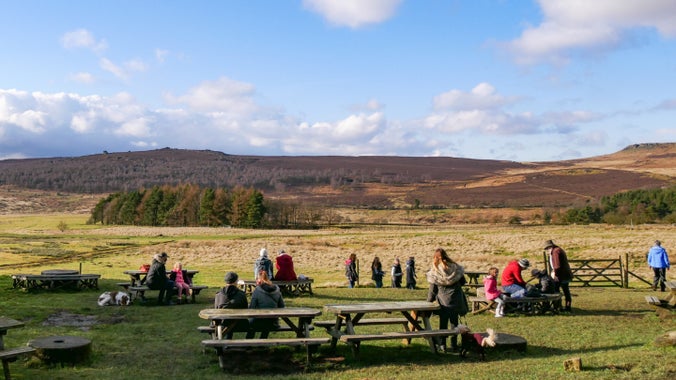 Visitors sitting at picnic benches outside the café at Longshaw, Derbyshire with a view of the moors in the background